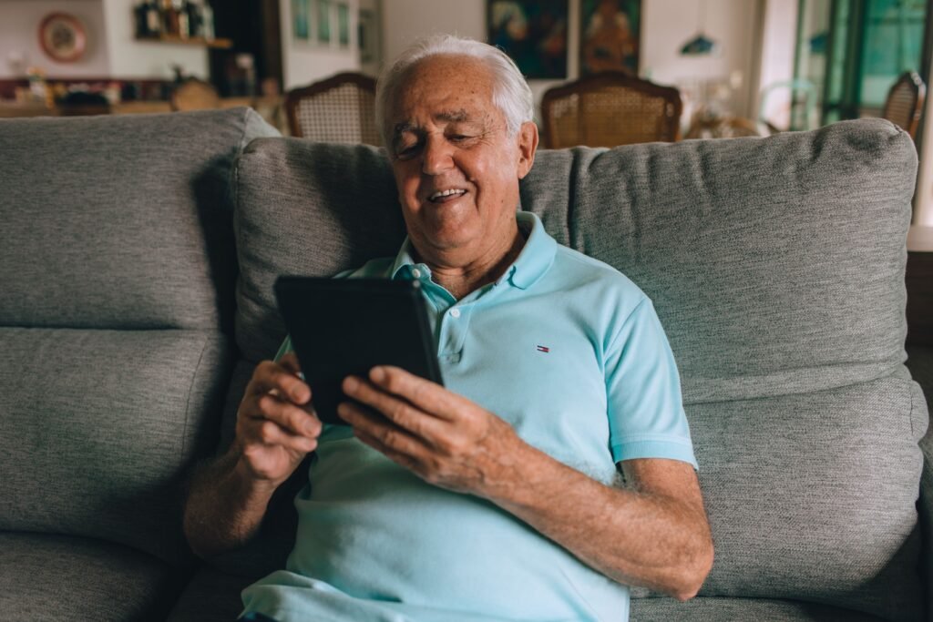 Smiling older man relaxing on the sofa with a tablet at home